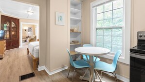 A room with a round table, two chairs, a bed, a wooden cabinet, a television, and a window with a view of greenery. - Carriage Cottage-  in the Heart of Everything Delaware (Delaware)