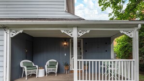 A porch with two wicker chairs, a small round table, and a white railing. - Carriage Cottage-  in the Heart of Everything Delaware (Delaware)
