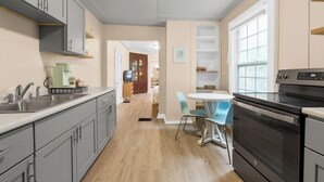 A kitchen with grey cabinets, a black stove, and a blue chair. - Carriage Cottage-  in the Heart of Everything Delaware (Delaware)