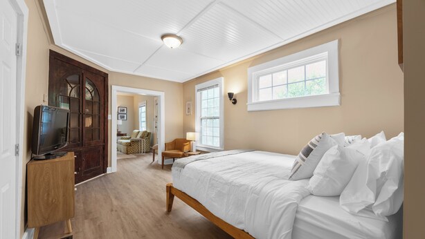 A bedroom with a wooden bed, a television on a stand, and a hallway leading to another room. - Carriage Cottage-  in the Heart of Everything Delaware (Delaware)