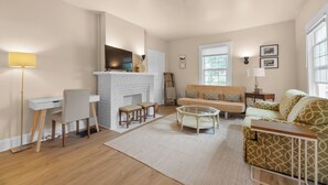 A living room with a white fireplace, a sofa, a coffee table, and a desk with a chair. - Carriage Cottage-  in the Heart of Everything Delaware (Delaware)