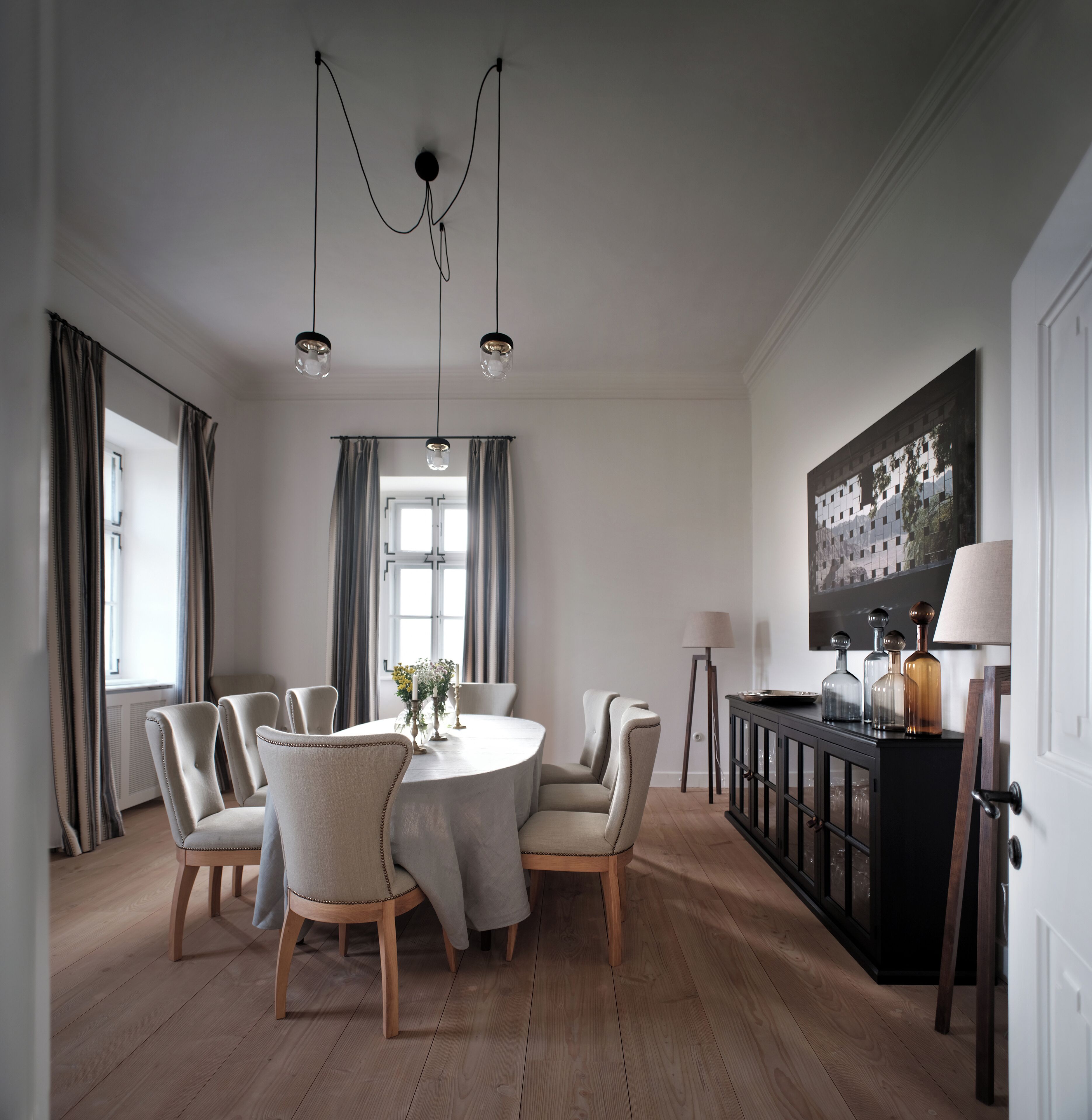 Un comedor con una mesa redonda, seis sillas y una araña. Hay un aparador negro con objetos decorativos encima.