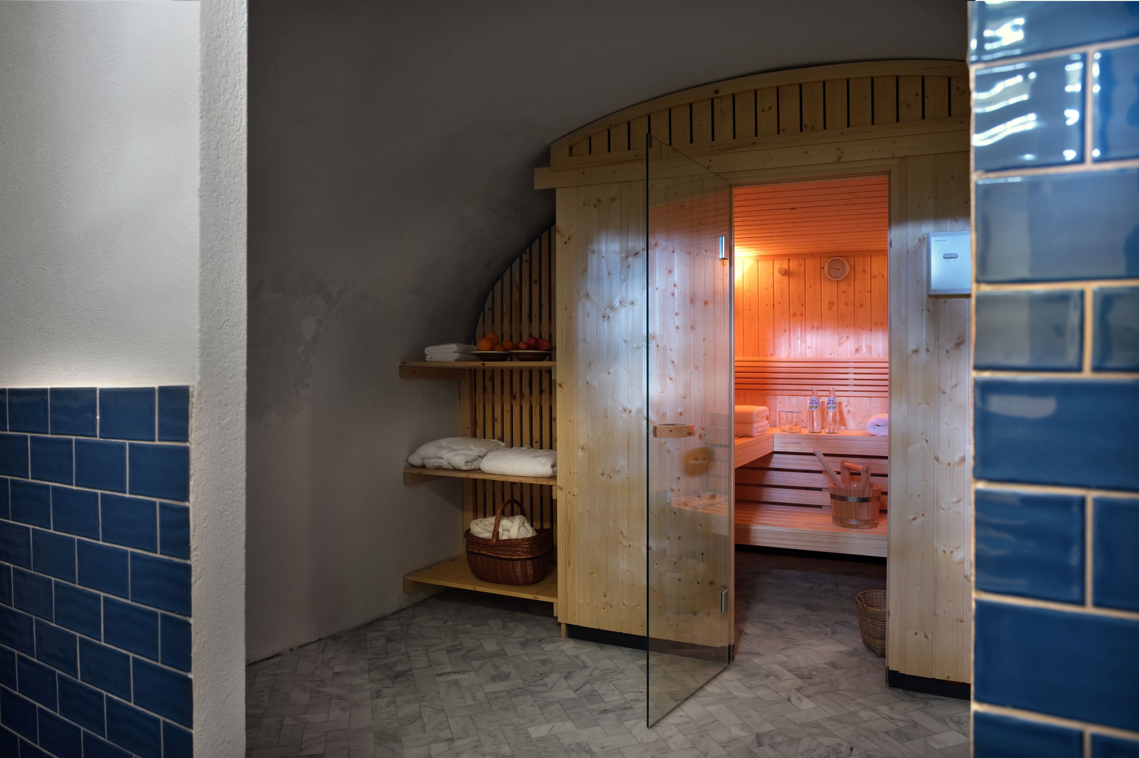 A sauna room with wooden walls, a glass door, and shelves with towels and baskets.
