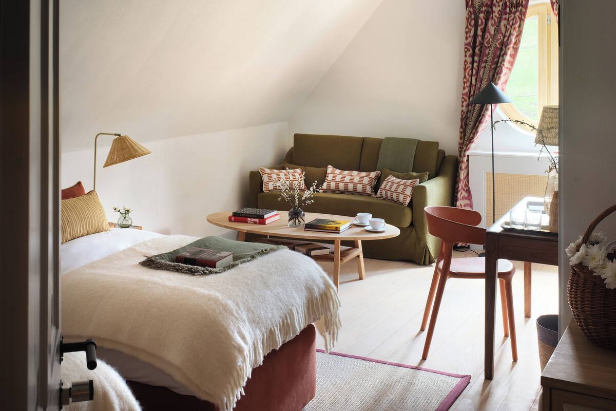 Um quarto aconchegante com uma cama, um sofá, uma mesa de jantar e uma janela com cortinas.
