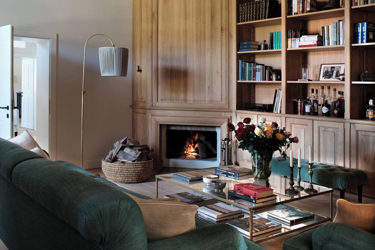 Uma sala de estar aconchegante com lareira, estante cheia de livros e assentos confortáveis.
