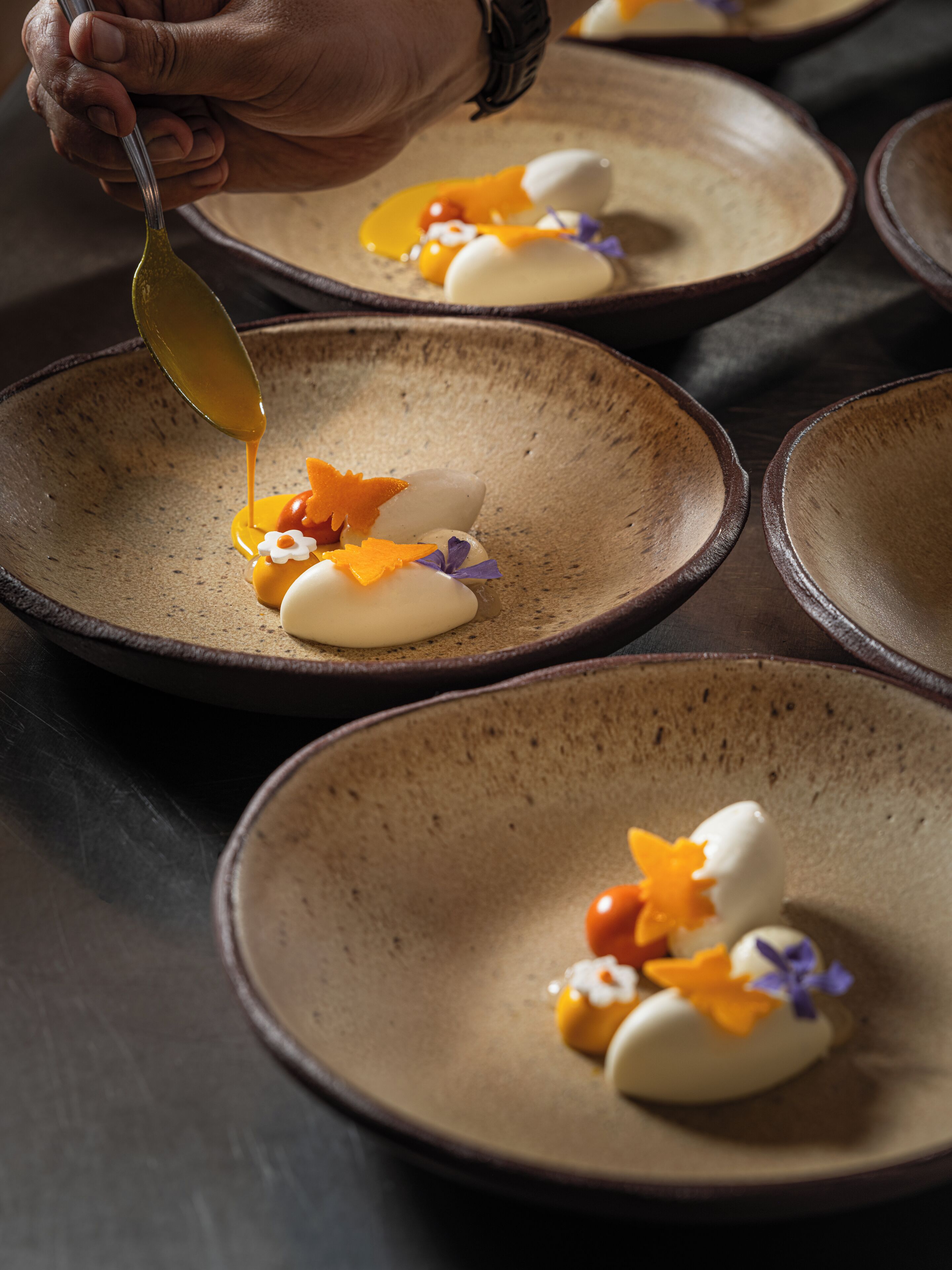 Une personne verse de la sauce sur un dessert, qui est présenté dans une assiette en céramique.