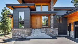 A modern two-story house with a stone foundation, wooden accents, and large windows. - Luxury Tahoe Estate | AC & Hot Tub | EV Charger| Golf Access, Near Lake & Trails (Truckee)