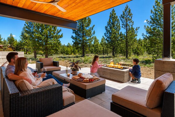 Un patio al aire libre con mobiliario de mimbre, un hogar para fogata y vistas a árboles.