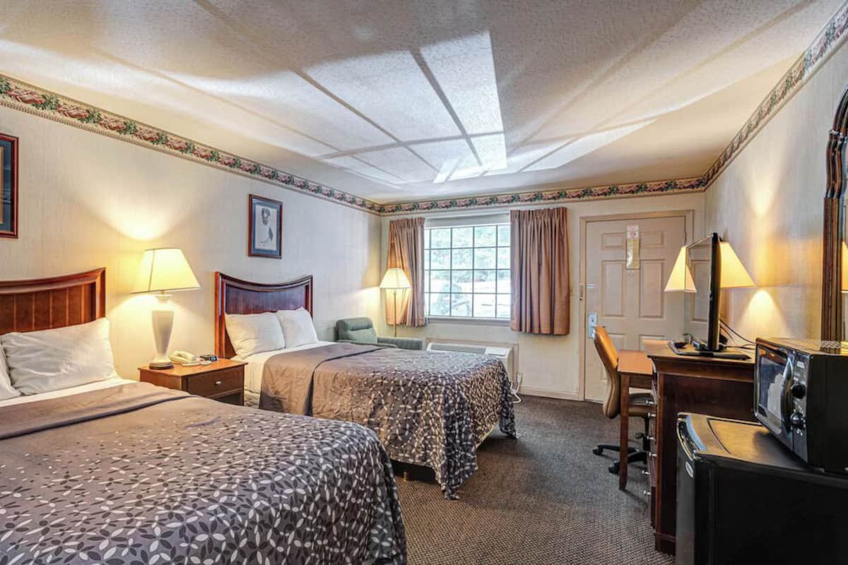 A hotel room with two beds, a desk, a chair, a television, and a window with curtains.
