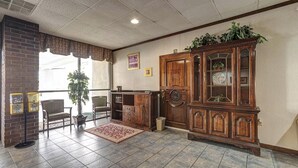 A lobby with a brick wall, a wooden cabinet with glass doors, a potted plant, and a tiled floor. - Northgate Inn by Townhouse Hattiesburg I-59 (Hattiesburg)