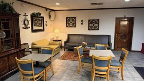 A room with a dining table, chairs, a sofa, a cabinet, and wall decorations. - Northgate Inn by Townhouse Hattiesburg I-59 (Hattiesburg)