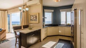 Une cuisine moderne avec un coin repas, de grandes fenêtres et une vue sur la mer.