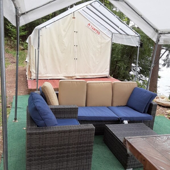 A covered outdoor seating area with a large white tent, wicker furniture, and a view of a body of water.