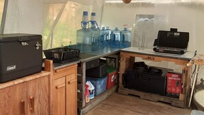 A compact kitchen area with a Coleman cooler, large water jugs, and a portable stove. - Tentrr-Riverfront Ritz (Lake Luzerne)