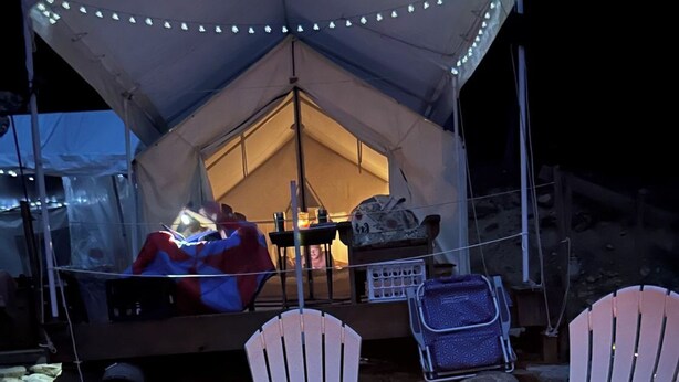 A tent with a fire pit and two white chairs in front. - Tentrr-Riverfront Ritz (Lake Luzerne)