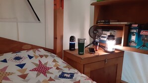 A bedroom with a bed, a bedside table with a lamp, a fan, and a box of books. - Tentrr-Riverfront Ritz (Lake Luzerne)