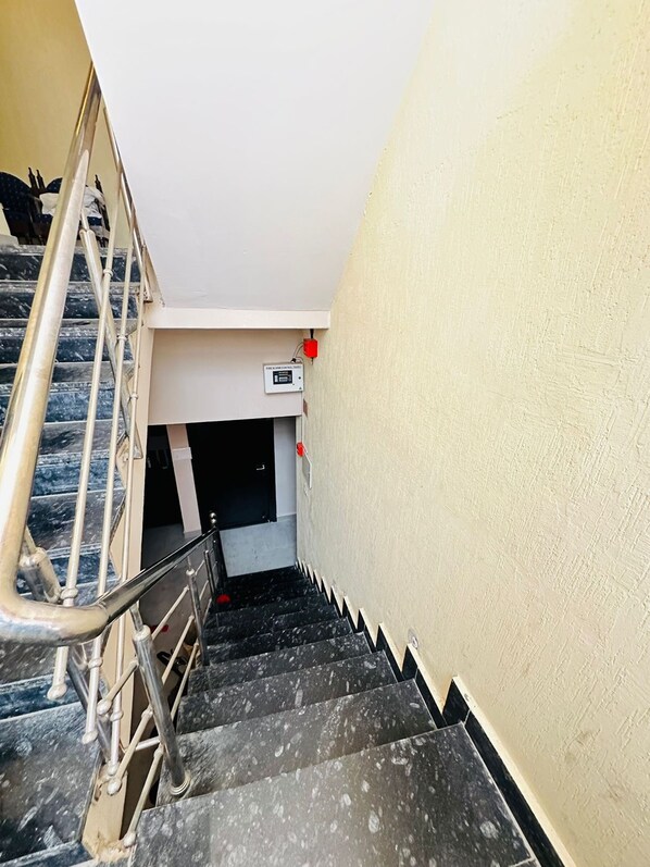 Un escalier avec une rampe, une boîte électrique fixée au mur et un feu rouge d’urgence.