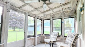 Een overdekte veranda met een plafondventilator, grote ramen en strepenstoelen.