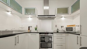 A modern kitchen with white cabinets, stainless steel appliances, and a black countertop. - 1 Bed South Quay Apartments Canary Wharf (London)