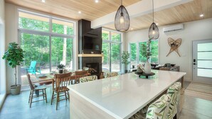Une cuisine spacieuse dotée d’un grand îlot central, d’un plafond en bois et de grandes fenêtres offrant une vue sur l’extérieur.