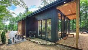 Une cabane moderne avec une façade en bois, de grandes fenêtres et une terrasse.