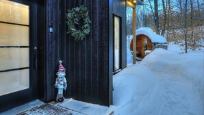 Un bâtiment moderne à l’extérieur sombre, doté d’une porte en bois et d’un toit recouvert de neige.