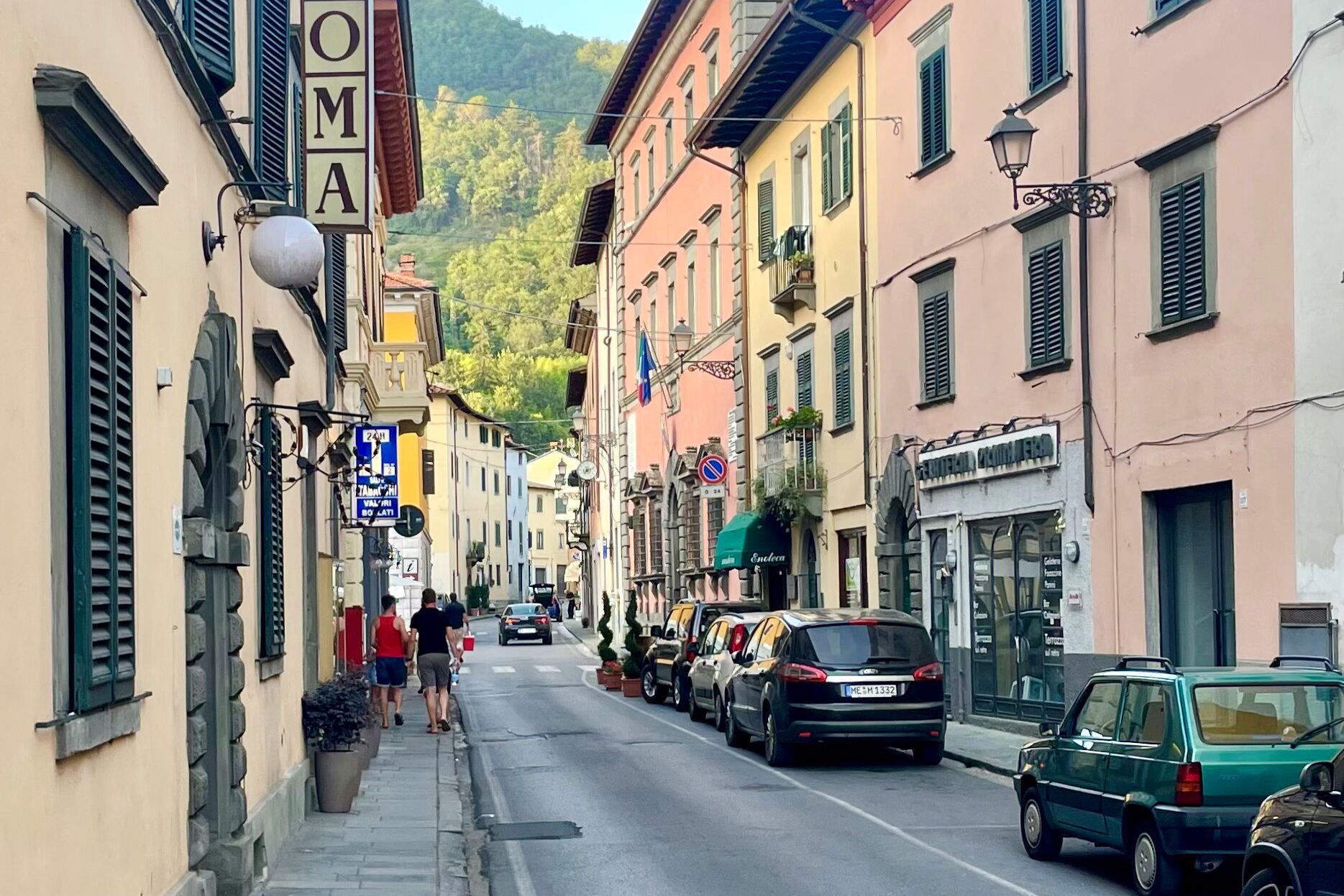 A narrow street lined with buildings, some with signs and storefronts, and parked cars.
