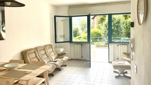 A living room with a sofa, a dining table with chairs, and a view through a large window.