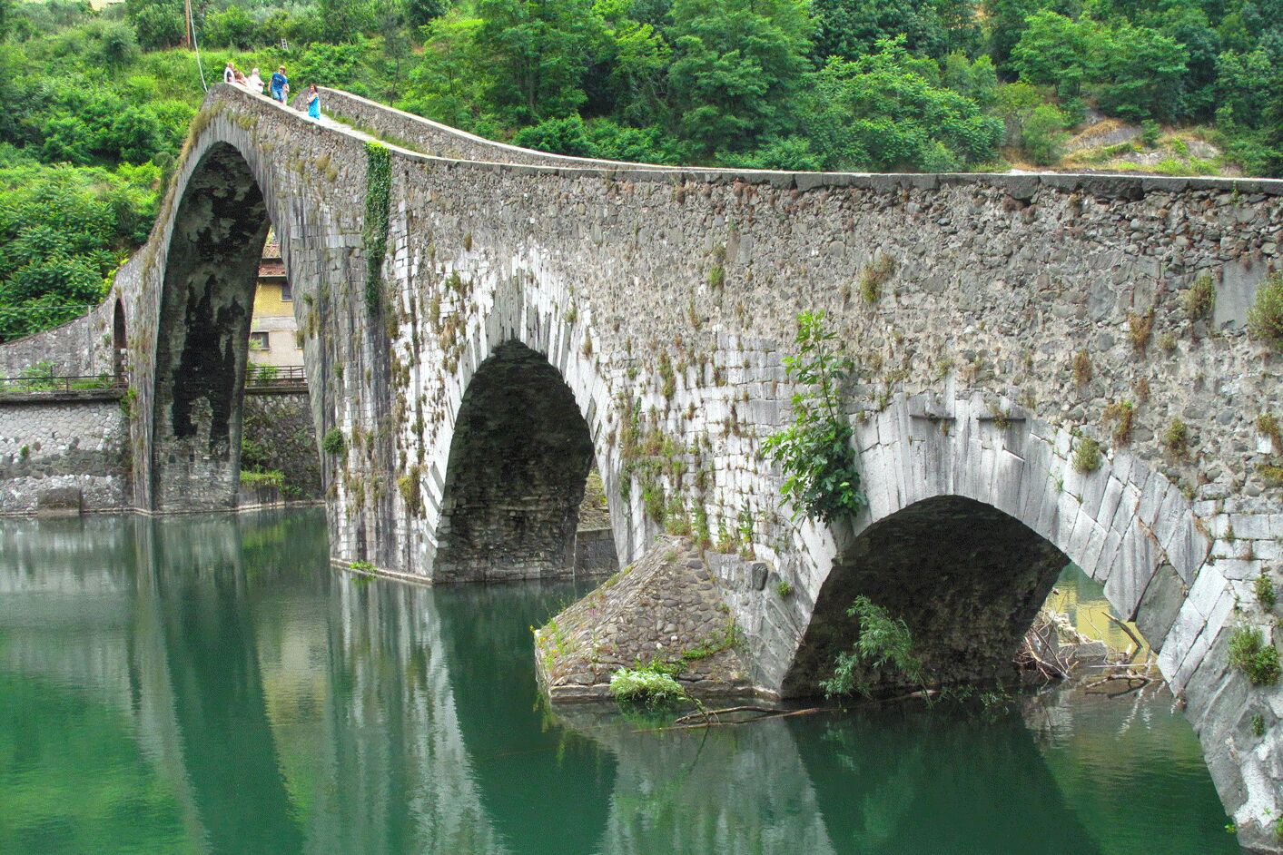 Eine Steinbrücke mit zwei Bögen über einem ruhigen Fluss, umgeben von üppiger Vegetation.
