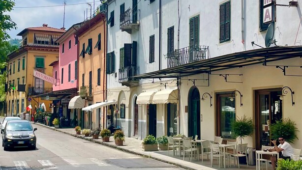 A row of colorful buildings with outdoor seating, a sign for a restaurant, and a parked car.