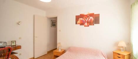 Un dormitorio con cama, mesitas de noche, un escritorio con silla, una lámpara colgante y un cuadro en la pared.