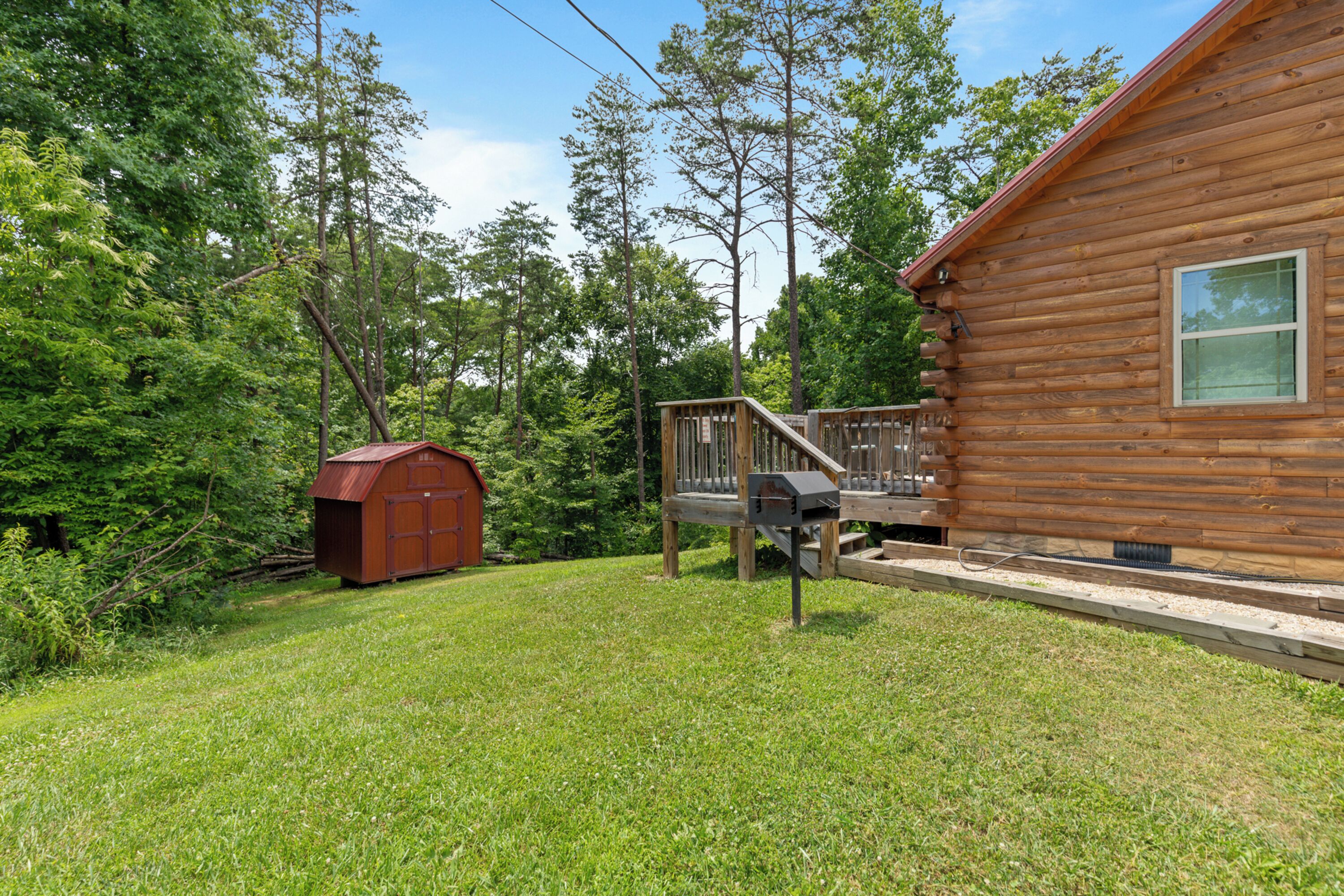 A wooden cabin with a deck and a small shed in a wooded area.