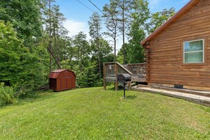 A wooden cabin with a deck and a small shed in a wooded area.
