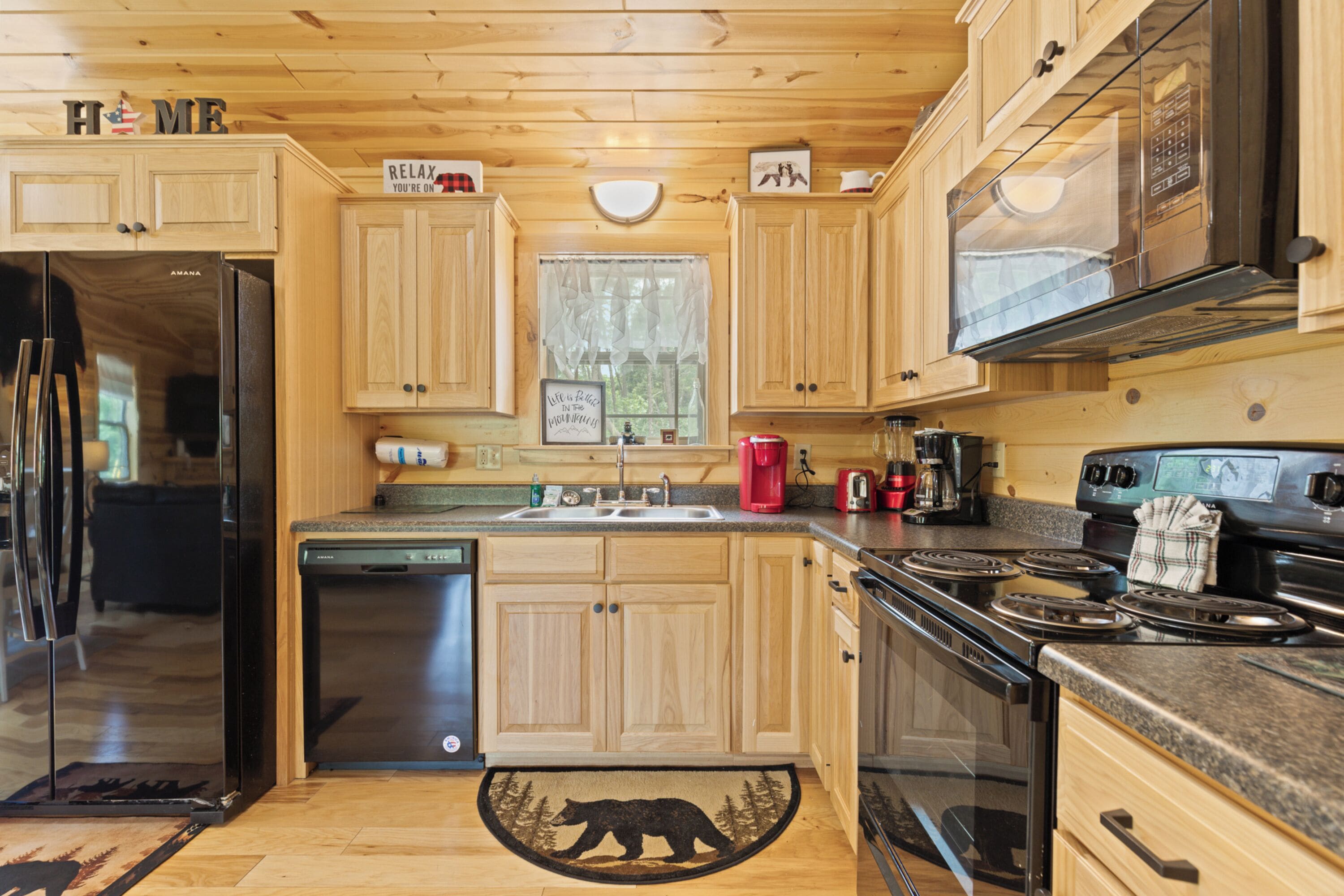 A modern kitchen with wooden cabinets, stainless steel appliances, and a bear-themed rug.