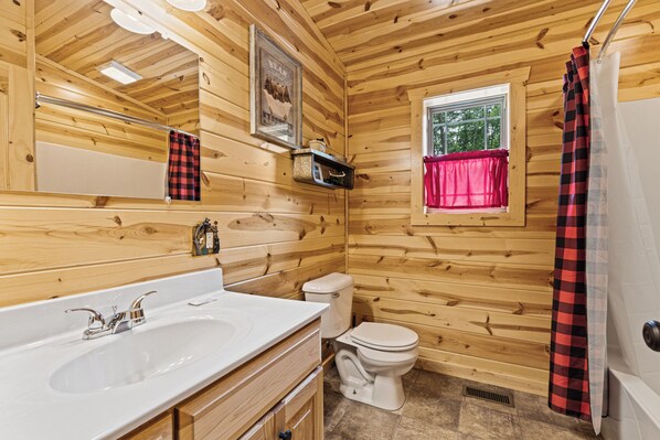 Een houten badkamer met een wastafel, toilet en raam.