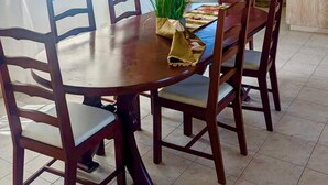 A dining area with a round wooden table and chairs, a kitchen in the background, and a ceiling fan. - Delightful-3 bedroom with AC and Wifi near Oistins, St Lawrence Gap (Christ Church)