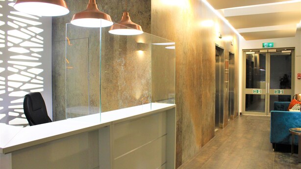A reception area with a glass partition, a reception desk, and a blue sofa. - One Bed Penthouse Apartment in City Road (London)