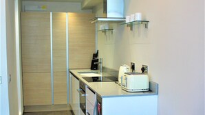 A compact kitchen with modern appliances, a dining area with a table set for two, and a small seating area. - One Bed Penthouse Apartment in City Road (London)