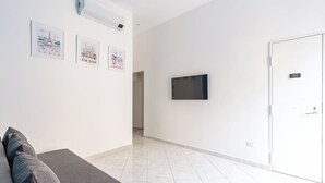 Ein modernes, minimalistisches Zimmer mit einem grauen Sofa, einem Flachbildfernseher an der Wand und einer weißen Tür.