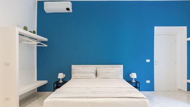 A bedroom with a bed, white nightstands, a white wardrobe, and a blue accent wall. - White&Blue Apartment at Sanità by Wonderful Italy (Naples)