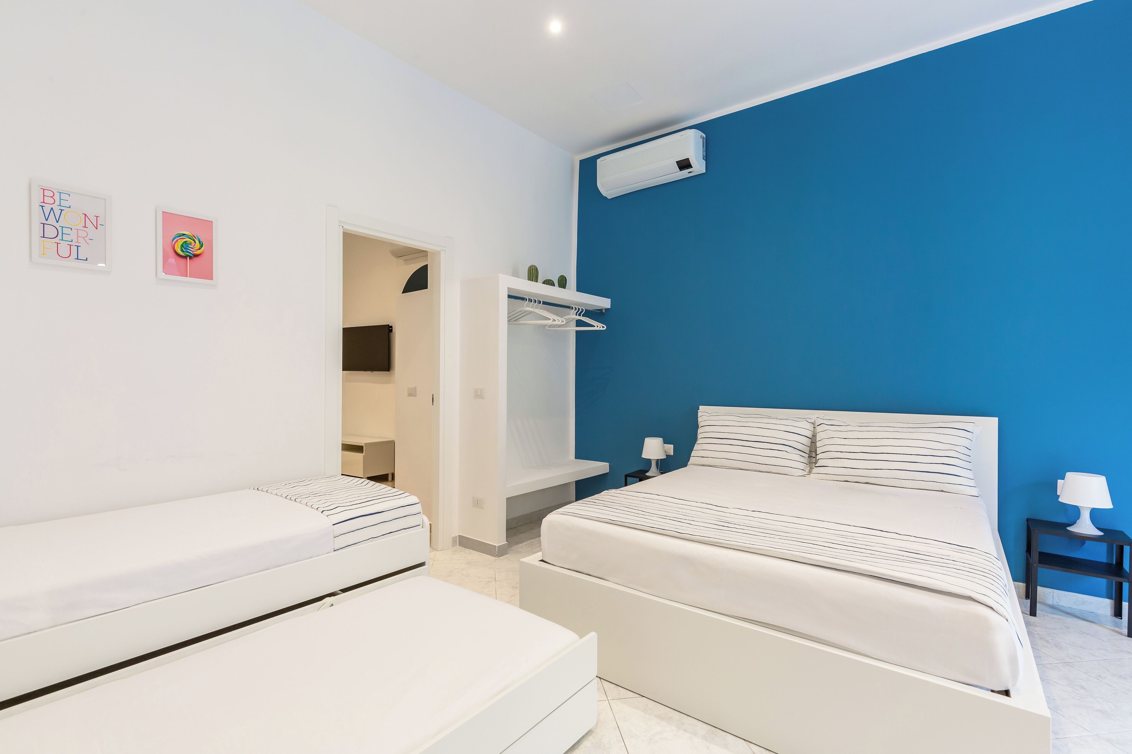 Une chambre avec un grand lit, un lit plus petit, un dressing et un mur d’accent bleu.