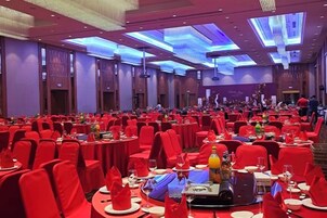 A banquet hall with round tables, red chairs, and a stage at the front.