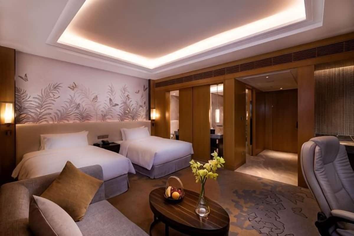 Ein Hotelzimmer mit zwei Betten, einem Sofa, einem kleinen Tisch mit einer Vase und einem Spiegel.
