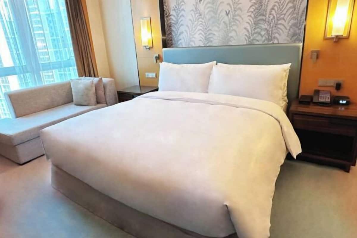 Ein großes Bett mit weißer Bettwäsche, ein Sofa mit Kissen, ein Nachttisch mit Telefon und ein Fenster mit Vorhängen.