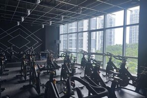 Une salle de sport équipée de vélos d’appartement et d’appareils de musculation, dotée de grandes fenêtres et d’un plafond haut.