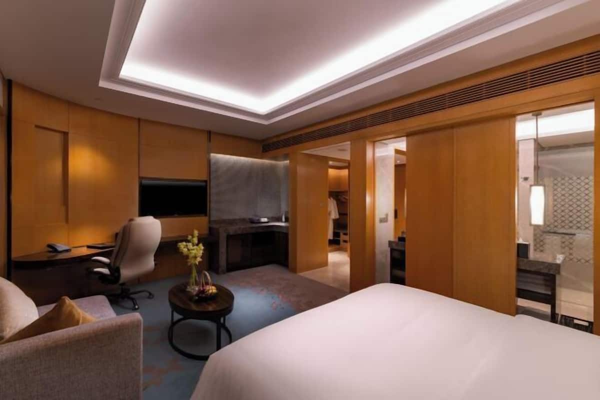 Ein Hotelzimmer mit Bett, Schreibtisch, Stuhl, einem kleinen Tisch mit Blumen und einem Fernseher.