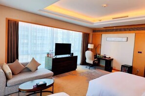 A hotel room with a sofa, a bed, a TV on a dresser, a desk with a chair, and a large window with curtains. - Yongkang World Trade International Hotel (Yongkang)