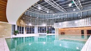 An indoor swimming pool with a curved ceiling and glass walls, surrounded by a wooden deck. - Yongkang World Trade International Hotel (Yongkang)