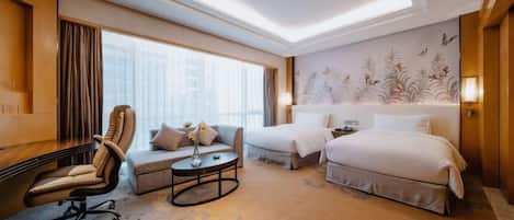 A hotel room with a desk, two beds, a sofa, and a large window.