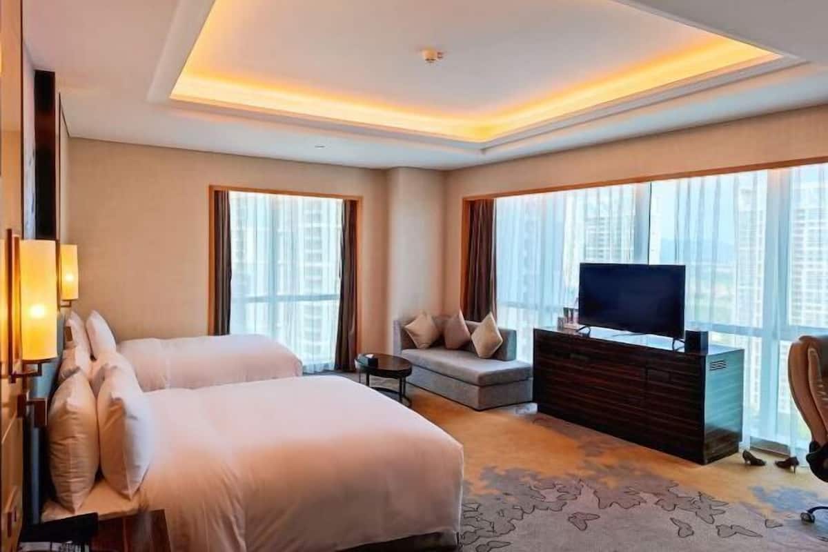 Ein Hotelzimmer mit einem großen Bett, einer Sitzecke, einem Fernseher auf einer Holzkommode und Blick auf die Stadt durch große Fenster.
